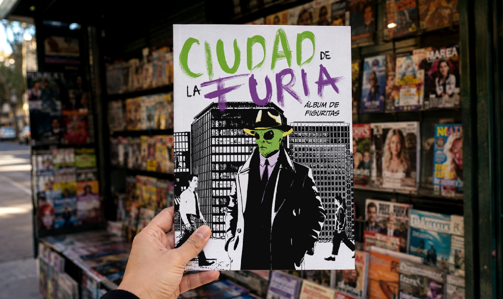 Tapa de Ciudad de la Furia sostenida frente a un local, mostrando una ilustración en blanco y negro sobre un fondo urbano.