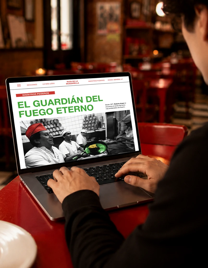 Mockup del suplemento Guerrin abierto en una computadora, presentado en el interior de una pizzería.