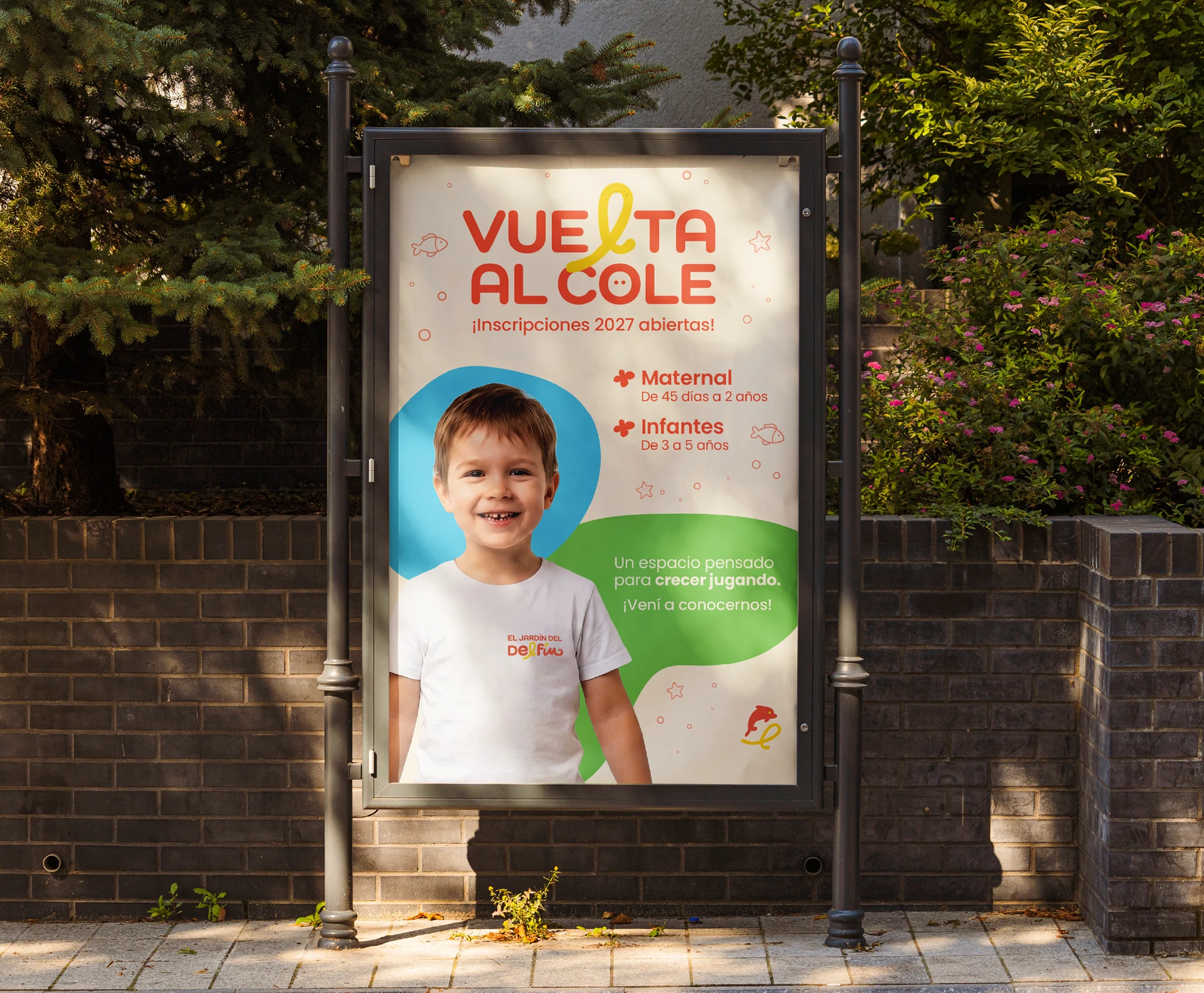 Cartel publicitario de El Jardín del Delfín instalado en exterior, con la fotografía de un niño y una composición gráfica colorida.