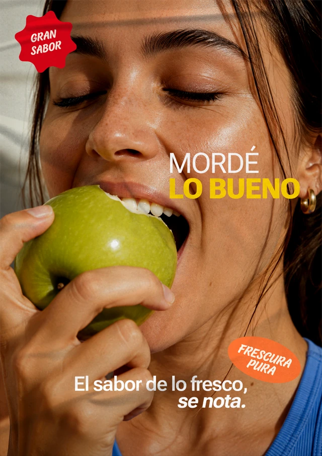Afiche publicitario de La Amistad con una mujer comiendo una fruta y el mensaje “Mordé lo bueno”, colocado sobre una pared en la vía pública.