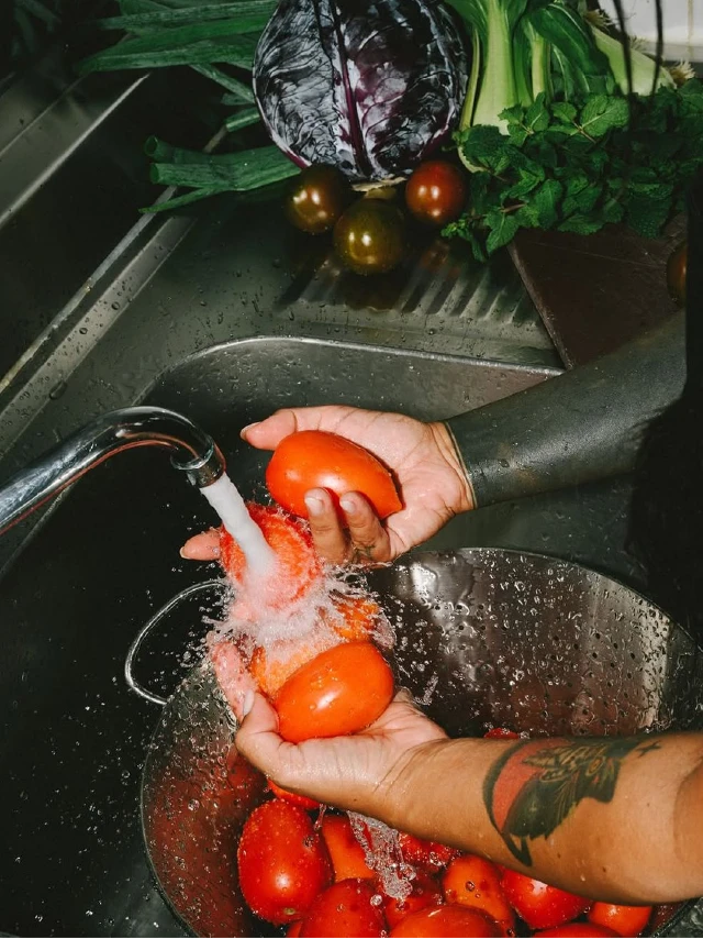 Fotografía de una persona lavando tomates y otras verduras frescas bajo el agua en una pileta